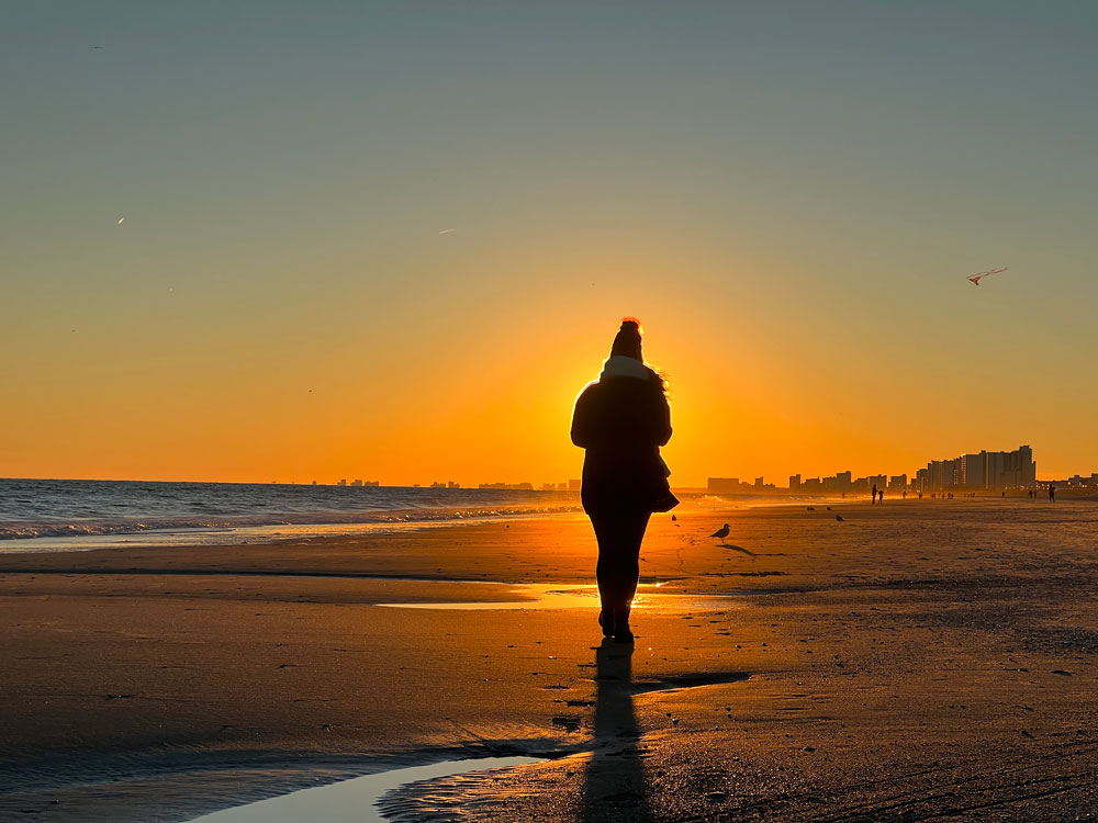 silhouette of person walking into sunset on beach