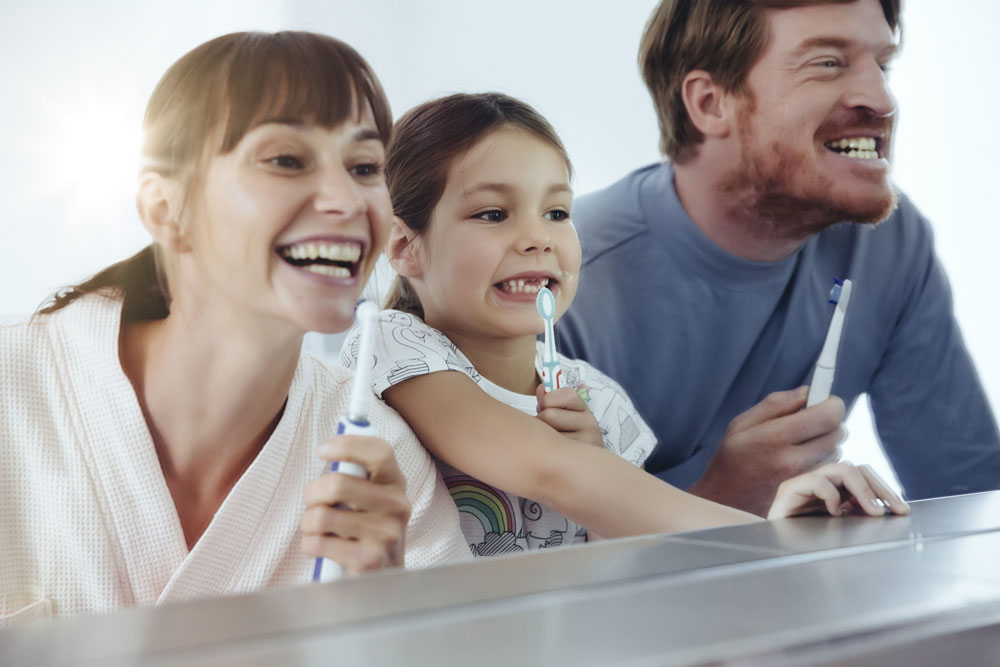 parents and young girl smile in mirror with toothbrushes