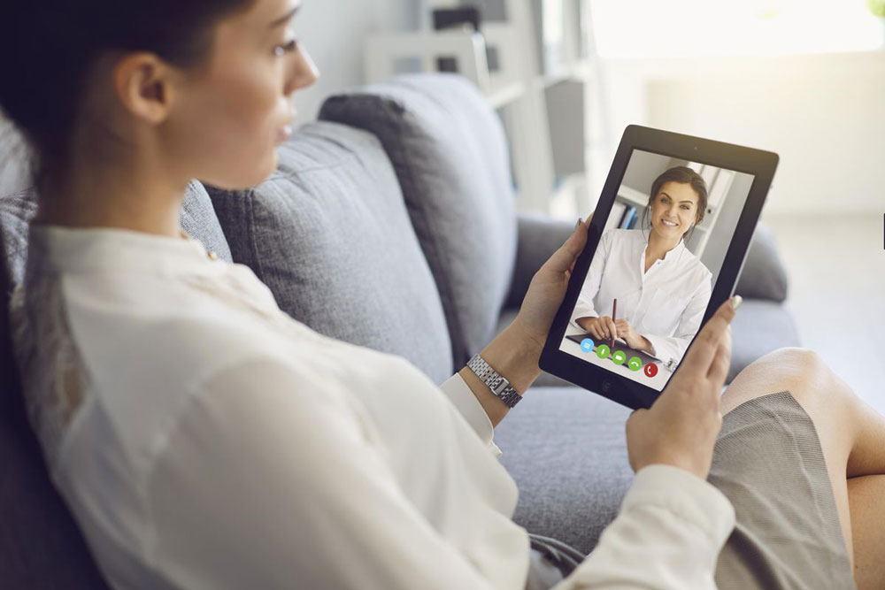 woman sitting on sofa talking to counselor on tablet