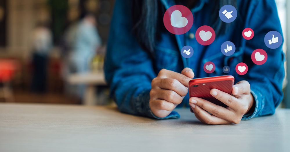 person holding cell phone with illustrations of hearts and likes floating around it