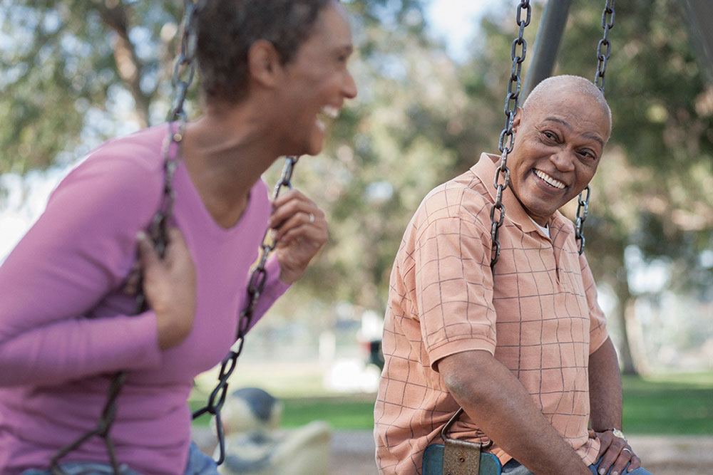 man and woman smile sitting on swingset