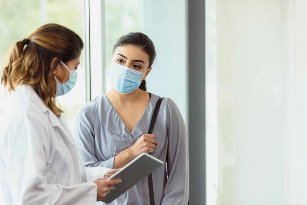 woman wearing mask talking with doctor in white coat in hallway