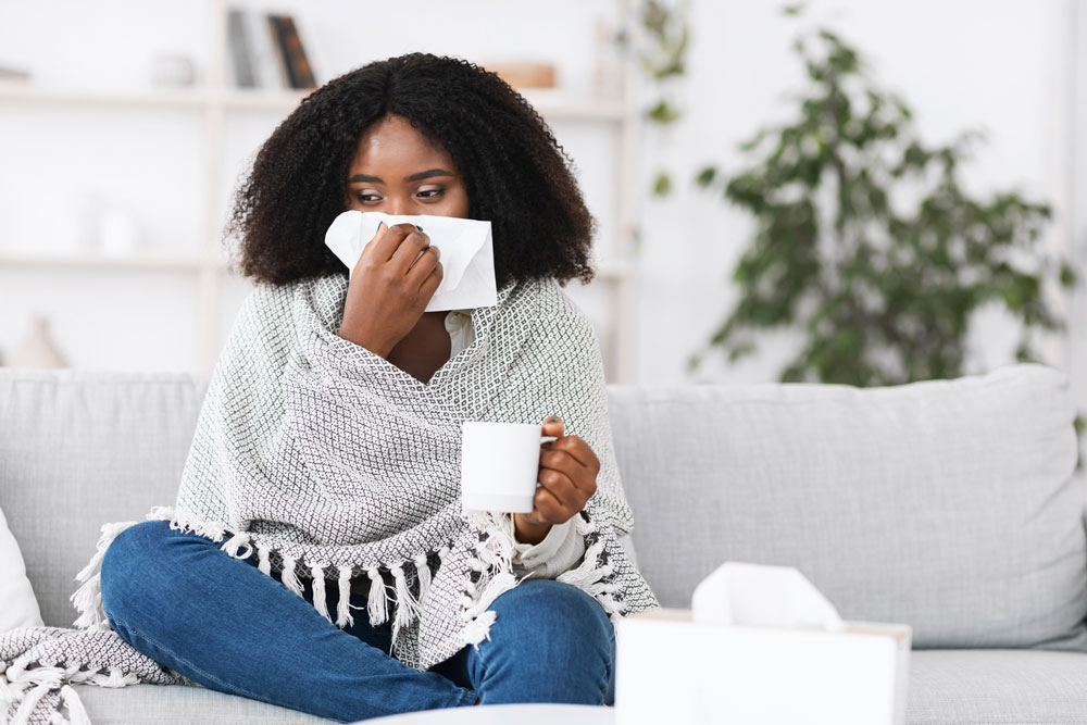 woman sitting on sofa with tissue over nose