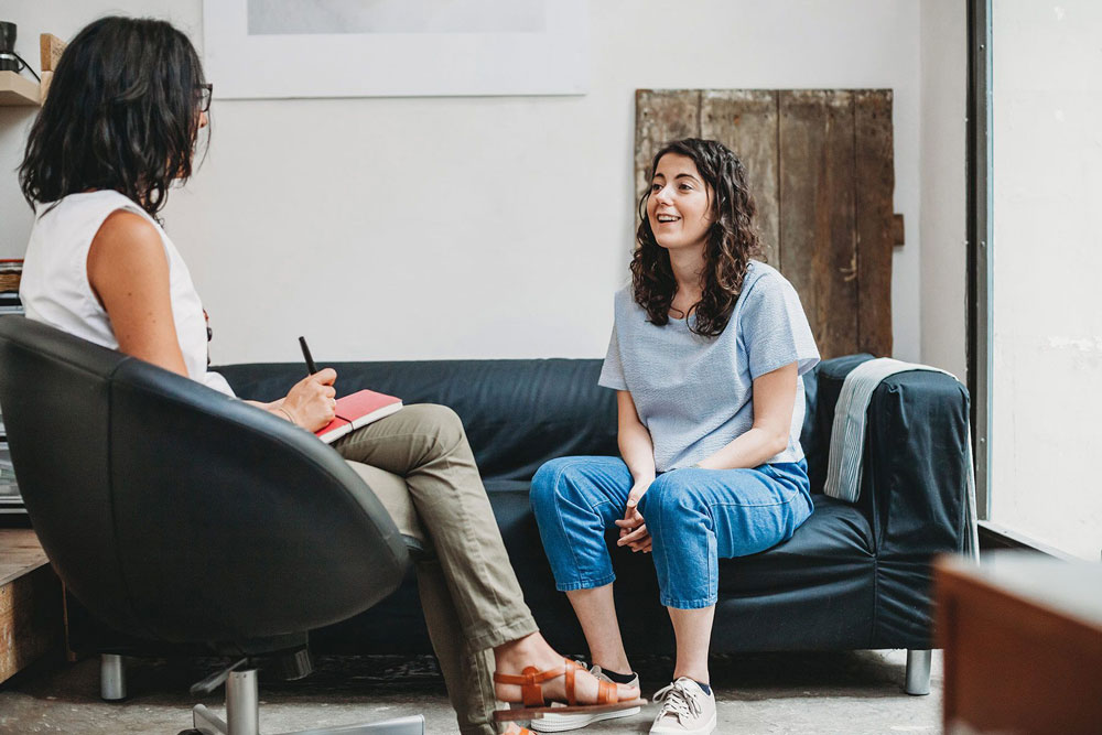 young woman sitting on couch talks with therapist taking notes