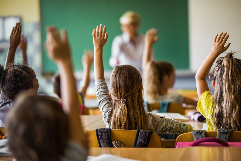 Children in classroom with hands in air