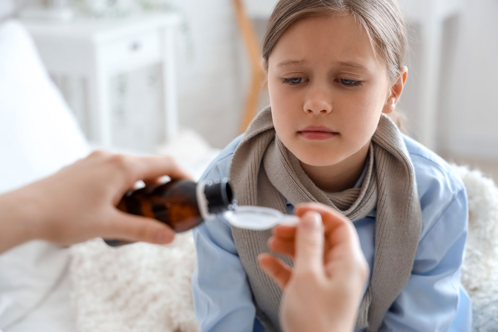 child sitting while adult hands pour liquid medication from bottle into spoon