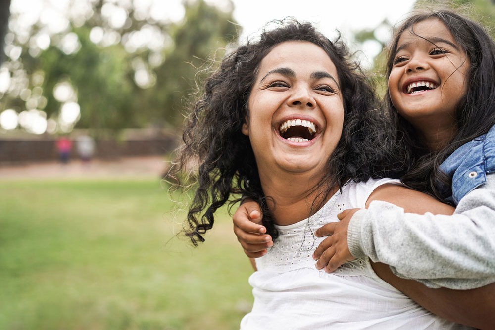 woman smiling with little girl on back outside in park